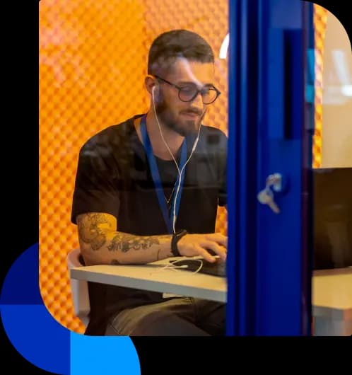 Colaborador do Asaas utiliza uma das cabines de reunião da sede. Ele está usando fones de ouvido enquanto mexe no computador.